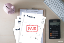 An invoice marked paid on a desk with a piggy bank and calculator